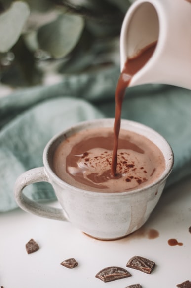 Hot chocolate pouring into white mug on white table
