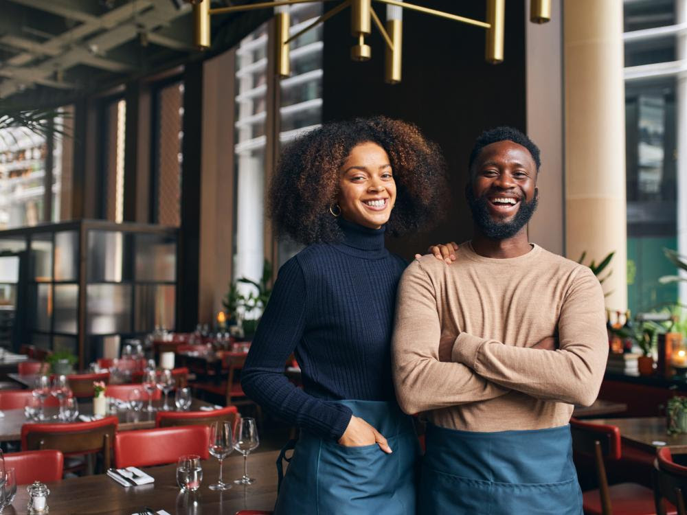 Two smiling people standing in a restaurant.