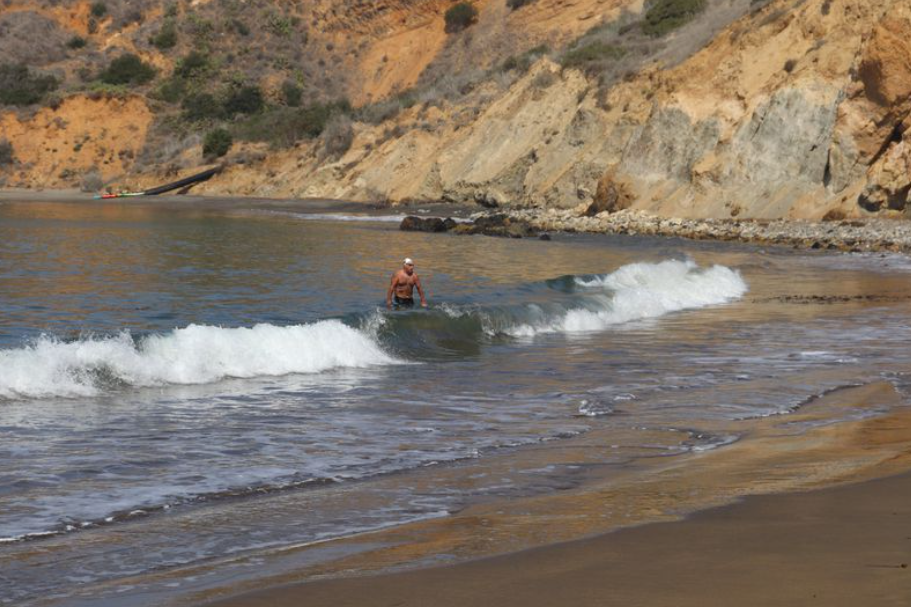 Man standing in surf on beach with mountains in background