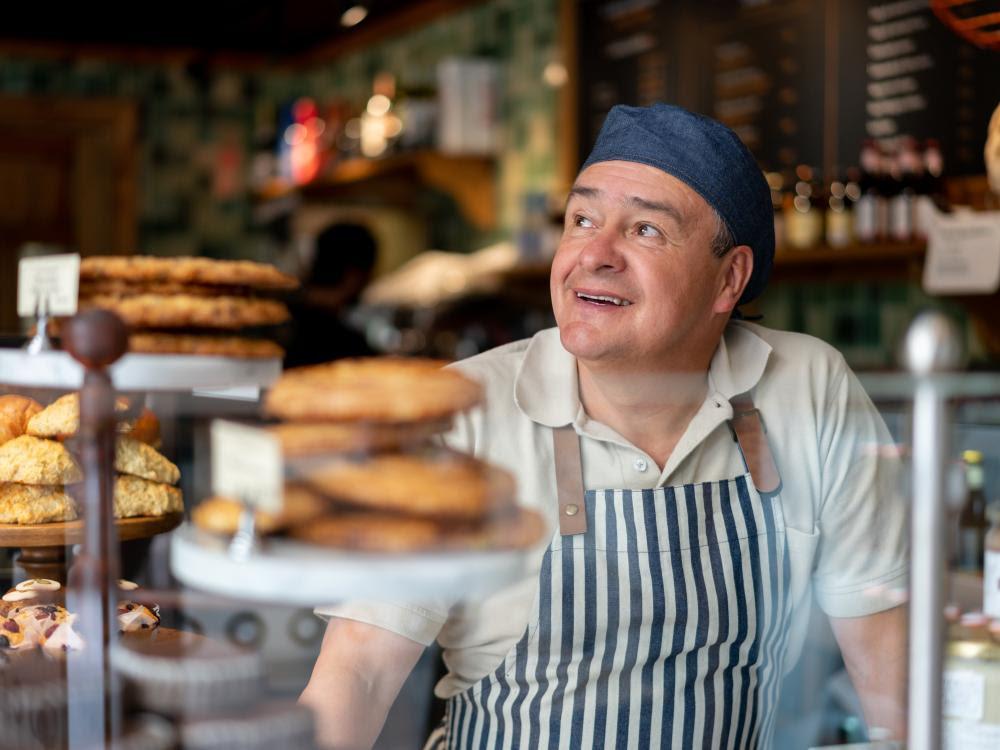 Baker standing by display case of baked goods.